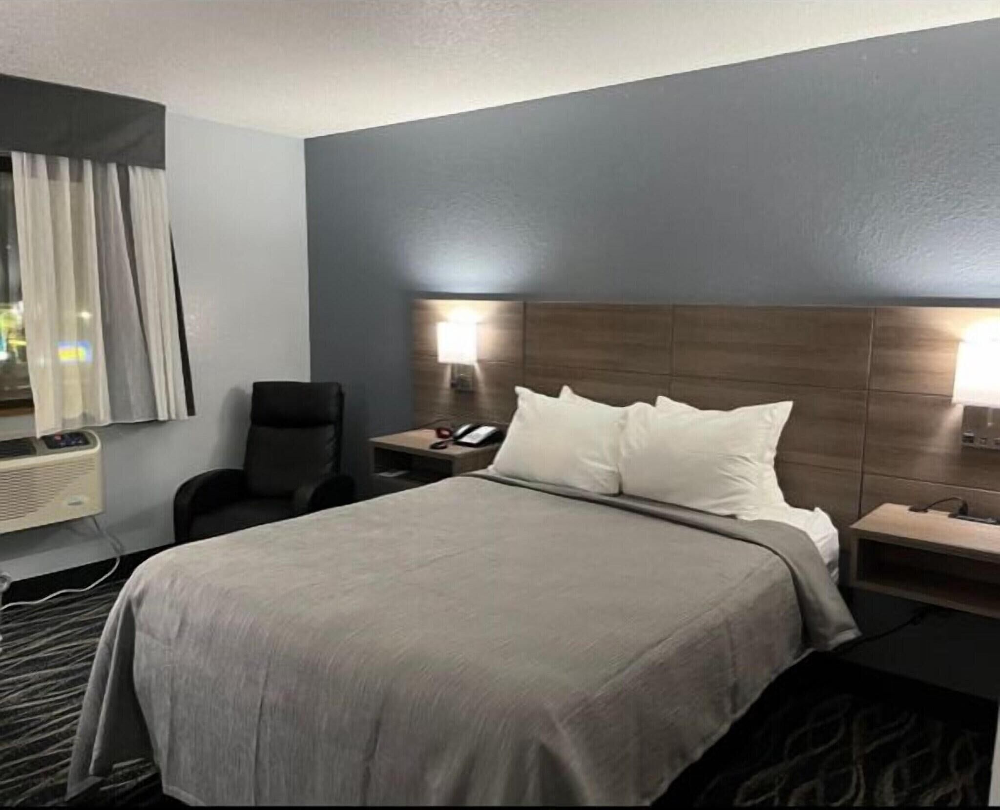 A hotel room with a bed, a chair, a desk with a lamp, and a phone.