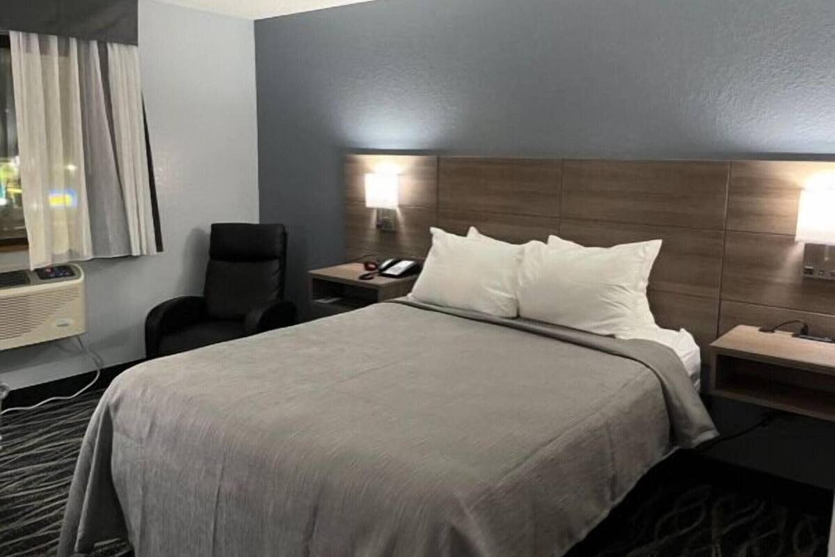 A hotel room with a bed, bedside tables, a chair, a desk, a lamp, and a window with curtains.