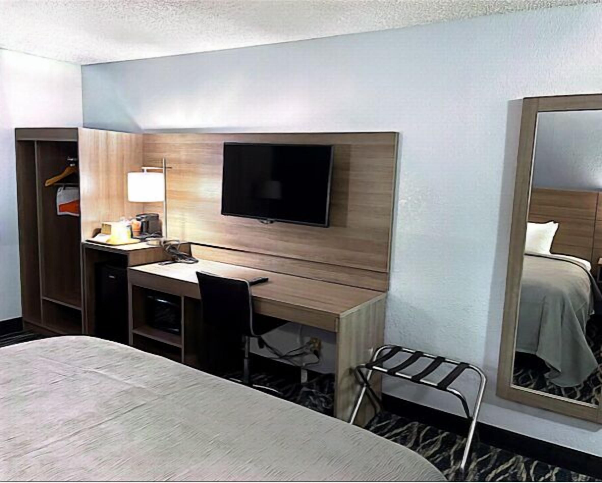 A hotel room with a bed, a desk with a chair, a television, a mirror, and a wardrobe.