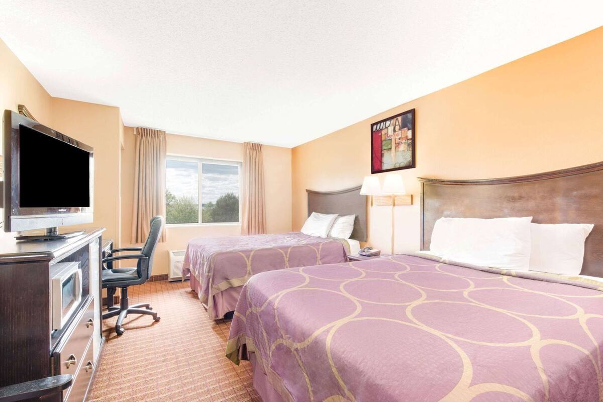 A hotel room with two beds, a TV, a desk, and a chair.