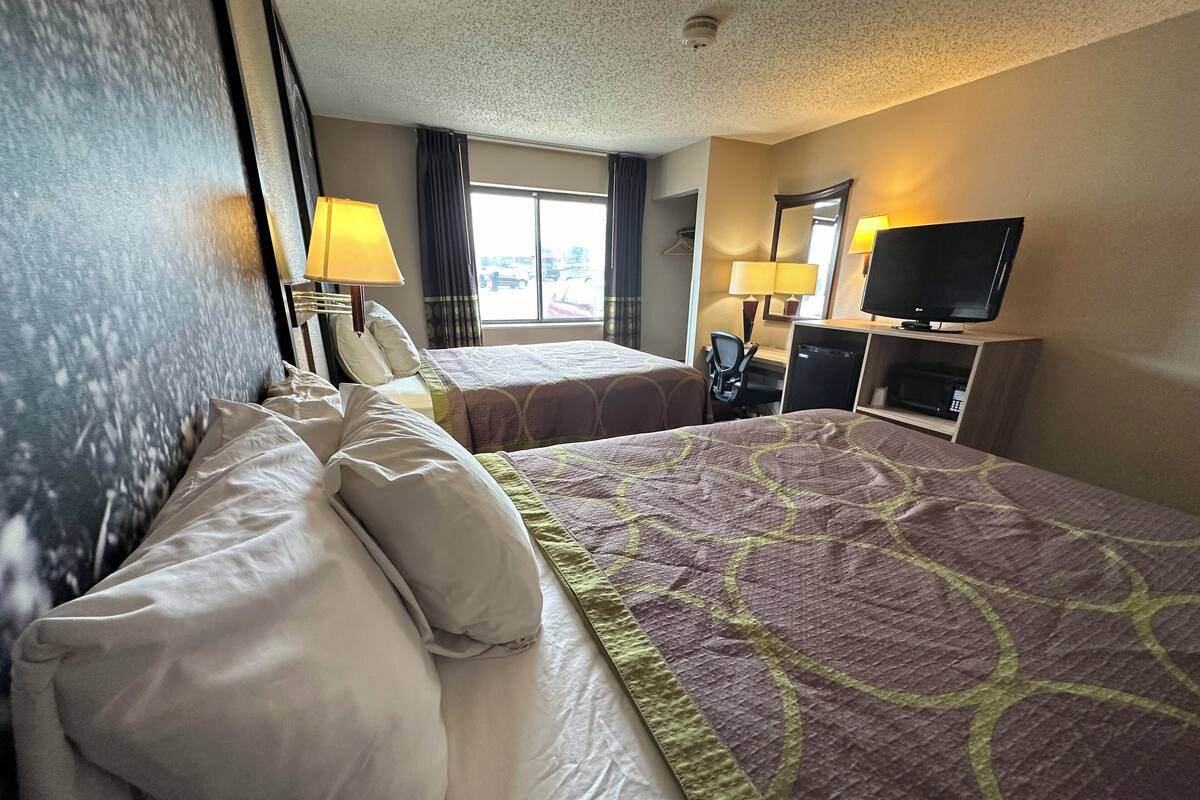 A hotel room with two beds, a desk, a television, and a window with curtains.