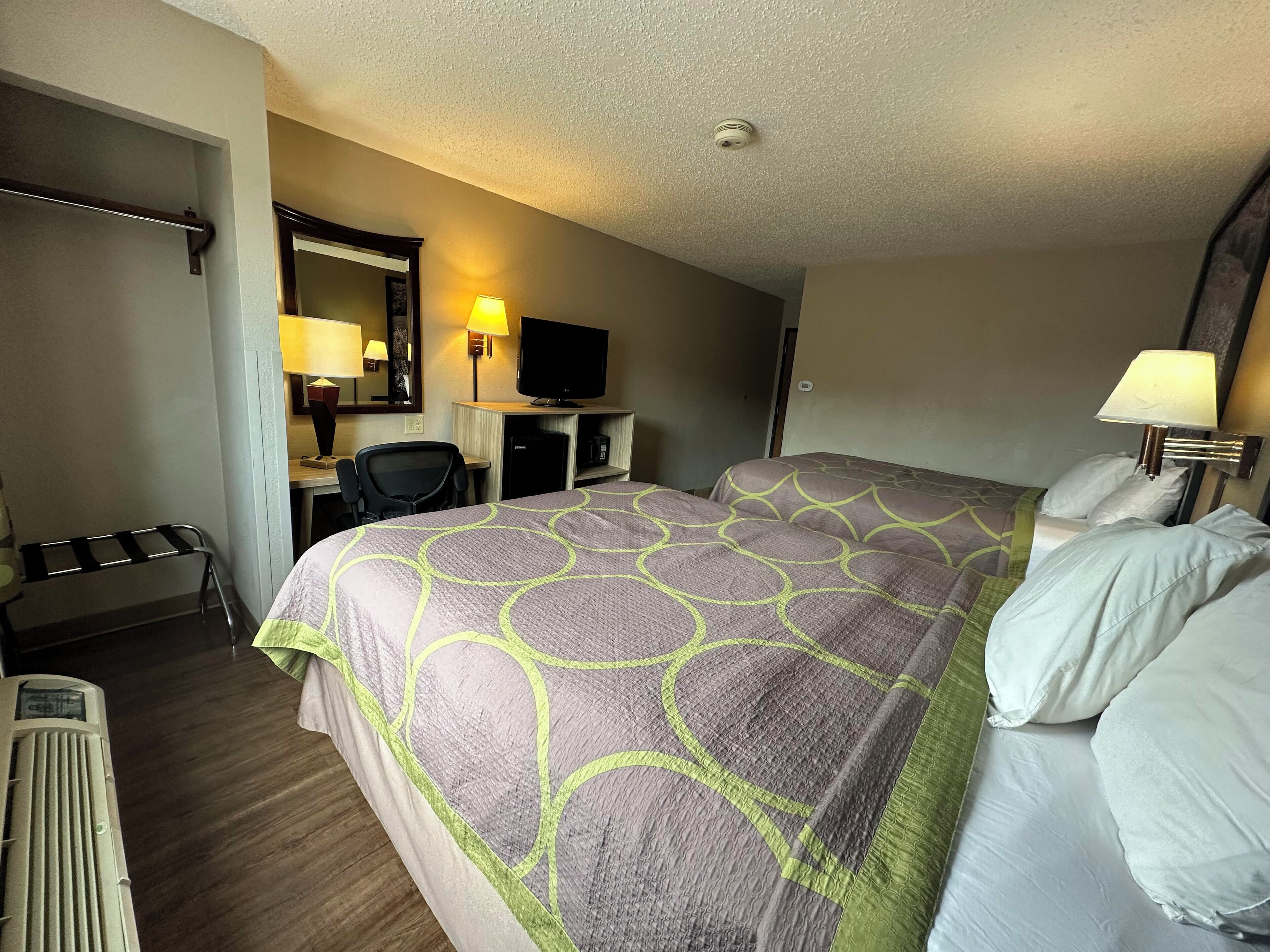 Una habitación de hotel con una cama grande, un escritorio con silla, un televisor y una lámpara.
