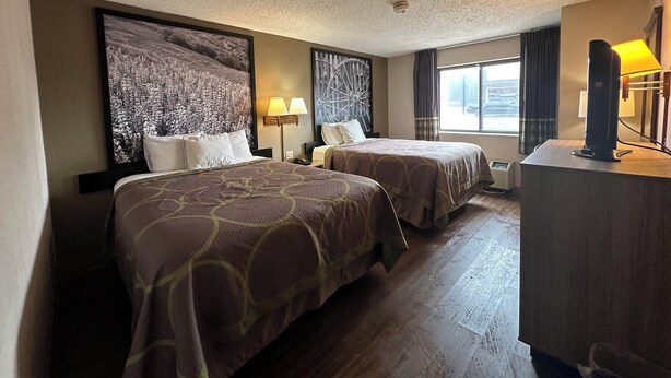 Habitación de hotel con dos camas, un mural grande en la pared, un escritorio con lámpara y una ventana con cortinas.