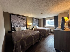 Habitación de hotel con dos camas, un mural grande en la pared, un escritorio con lámpara y una ventana con cortinas.
