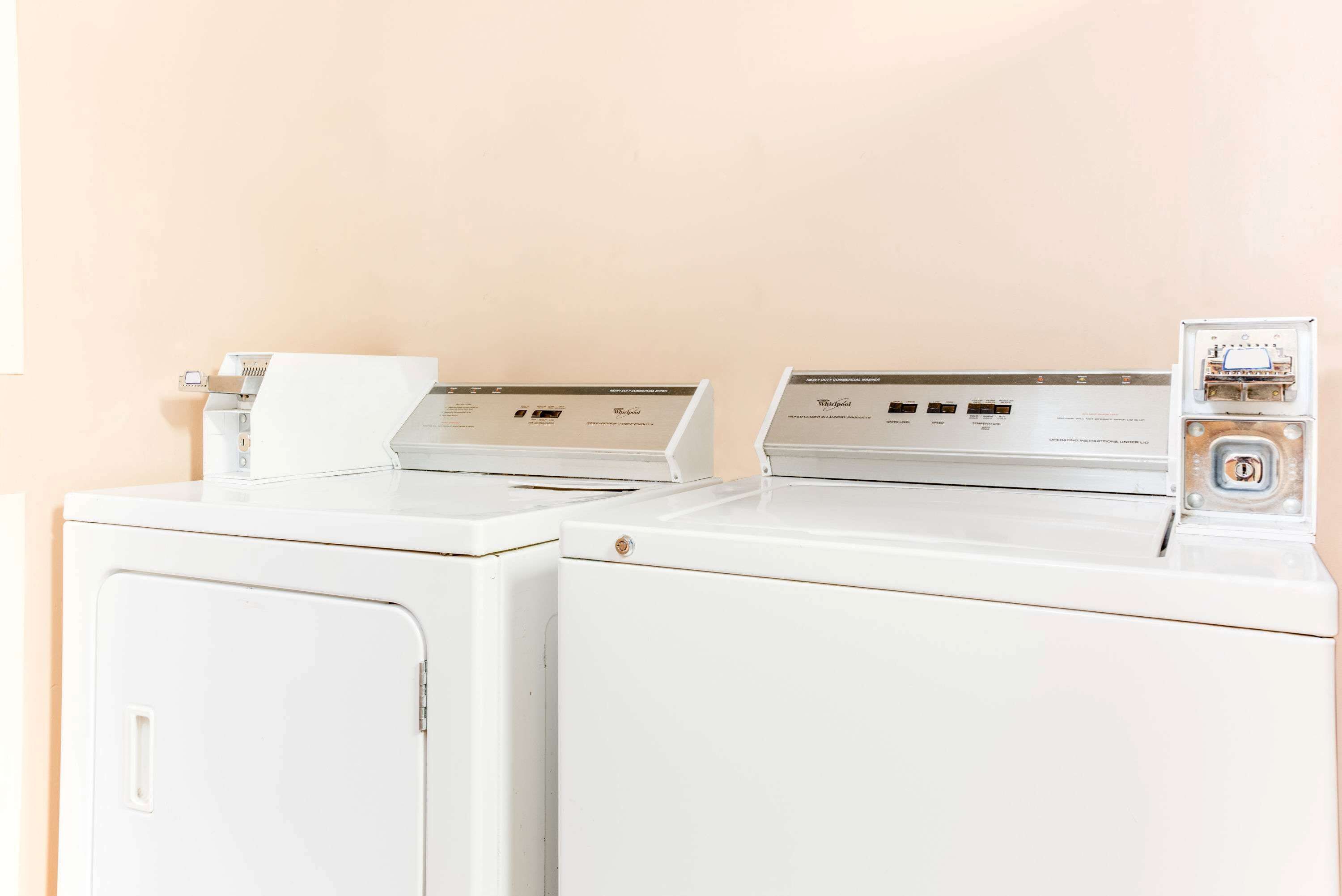 Two white front-loading washing machines with control panels, a power outlet, and a wall-mounted electrical box.