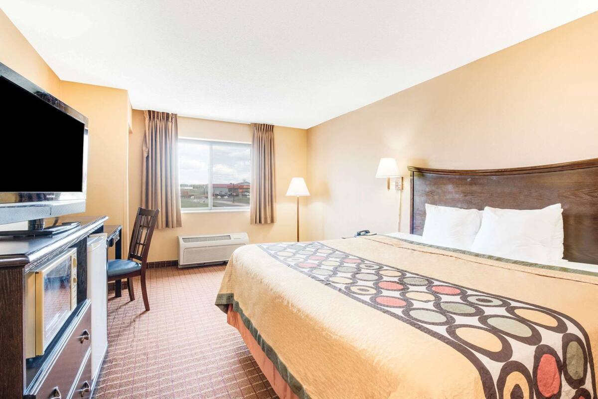A hotel room with a bed, a TV, a desk, a chair, a window, and an air conditioner.