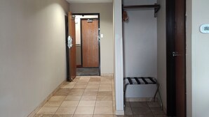 Un pasillo con suelo de baldosas, una puerta de madera, un perchero y un termostato en la pared.