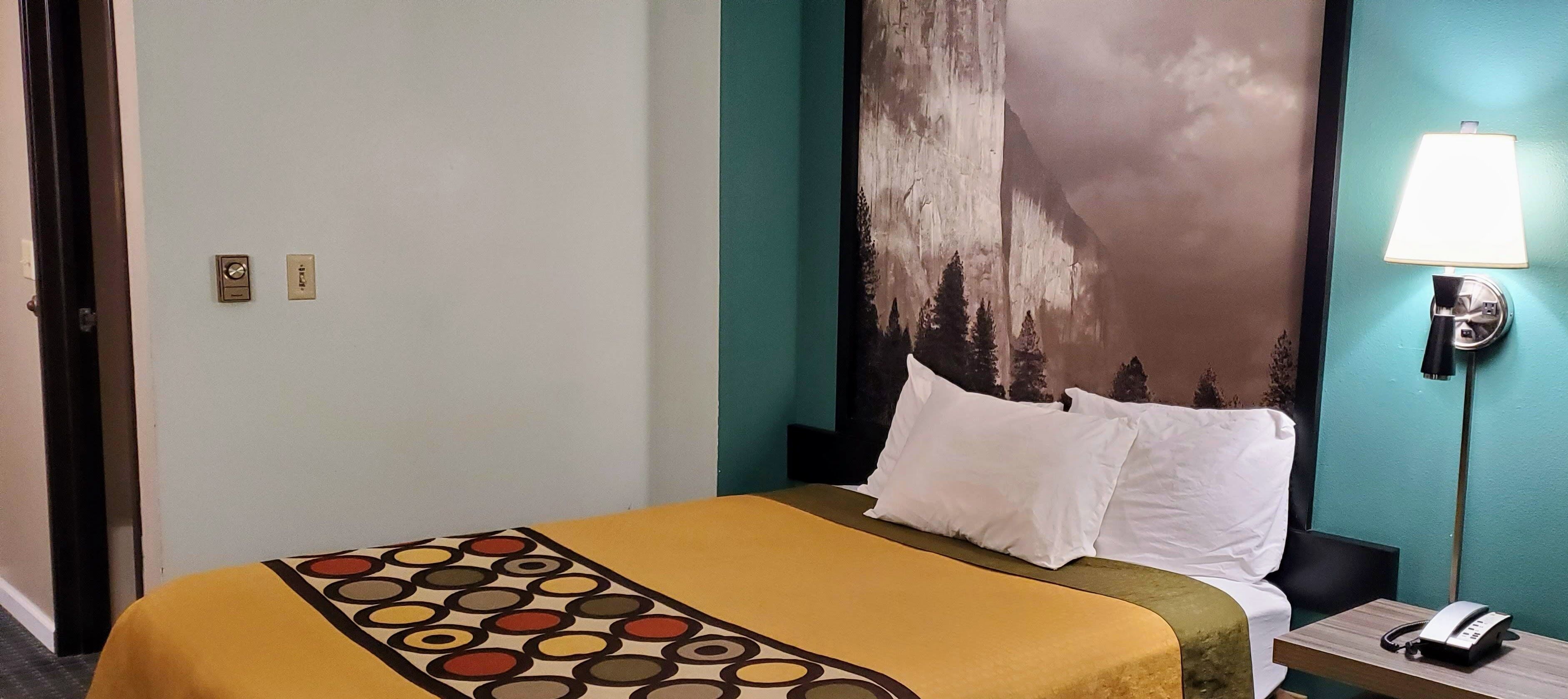 Ein Hotelzimmer mit einem Bett, einem Nachttisch mit Lampe und einem Wandbild von einem Berg.