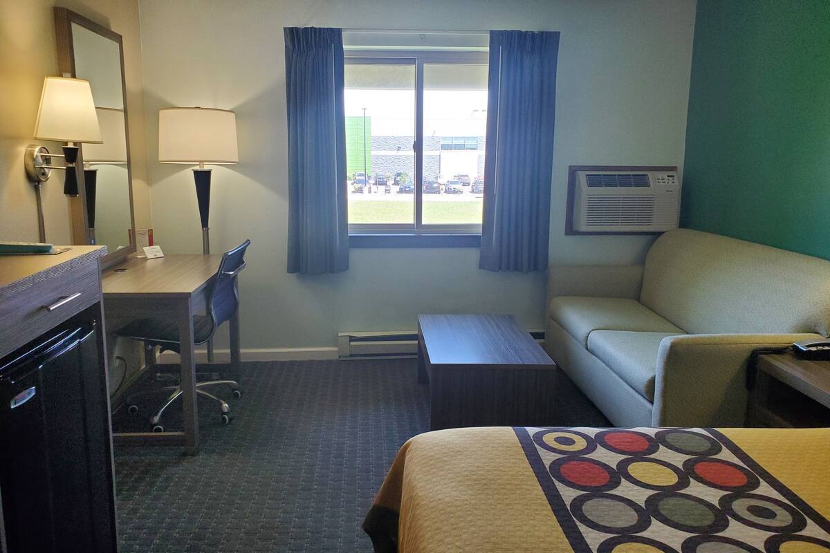 A hotel room with a desk, chair, bed, and a window with curtains.