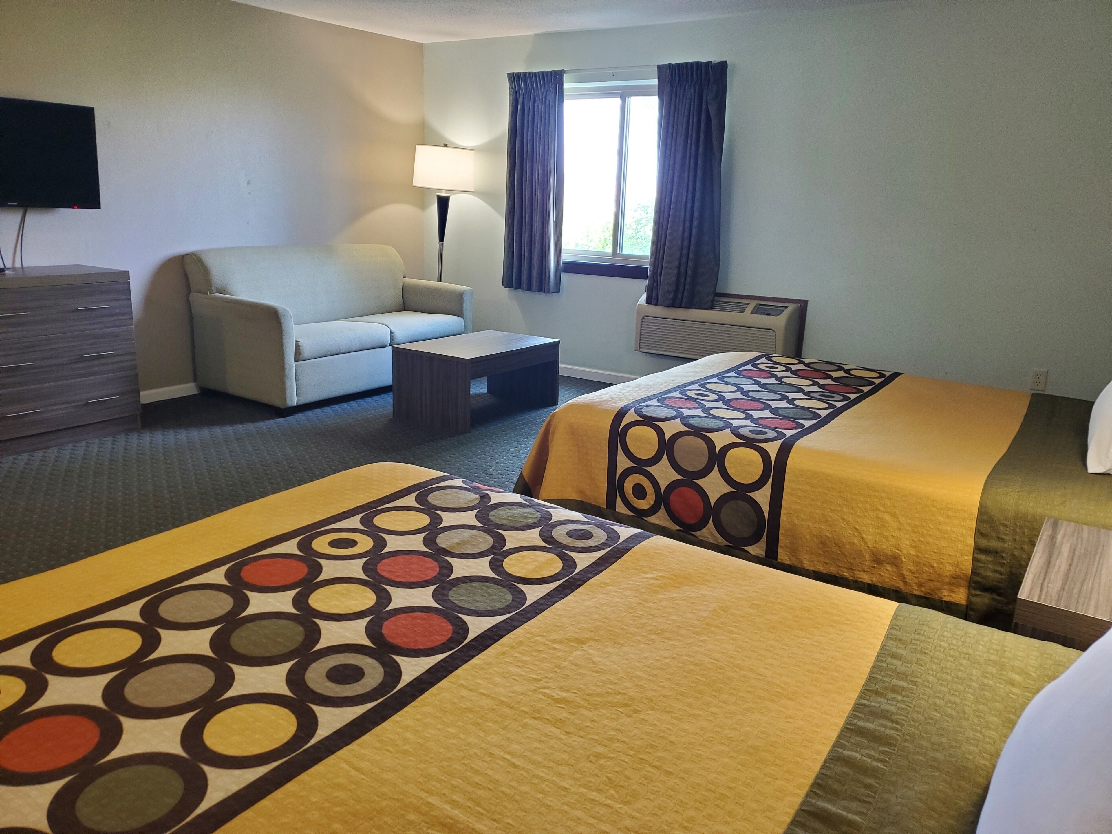 A hotel room with two beds, a sofa, a coffee table, a TV, and a window with curtains.
