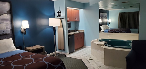 A hotel room with a bed, a desk, a bathroom with a bathtub, and a kitchenette.