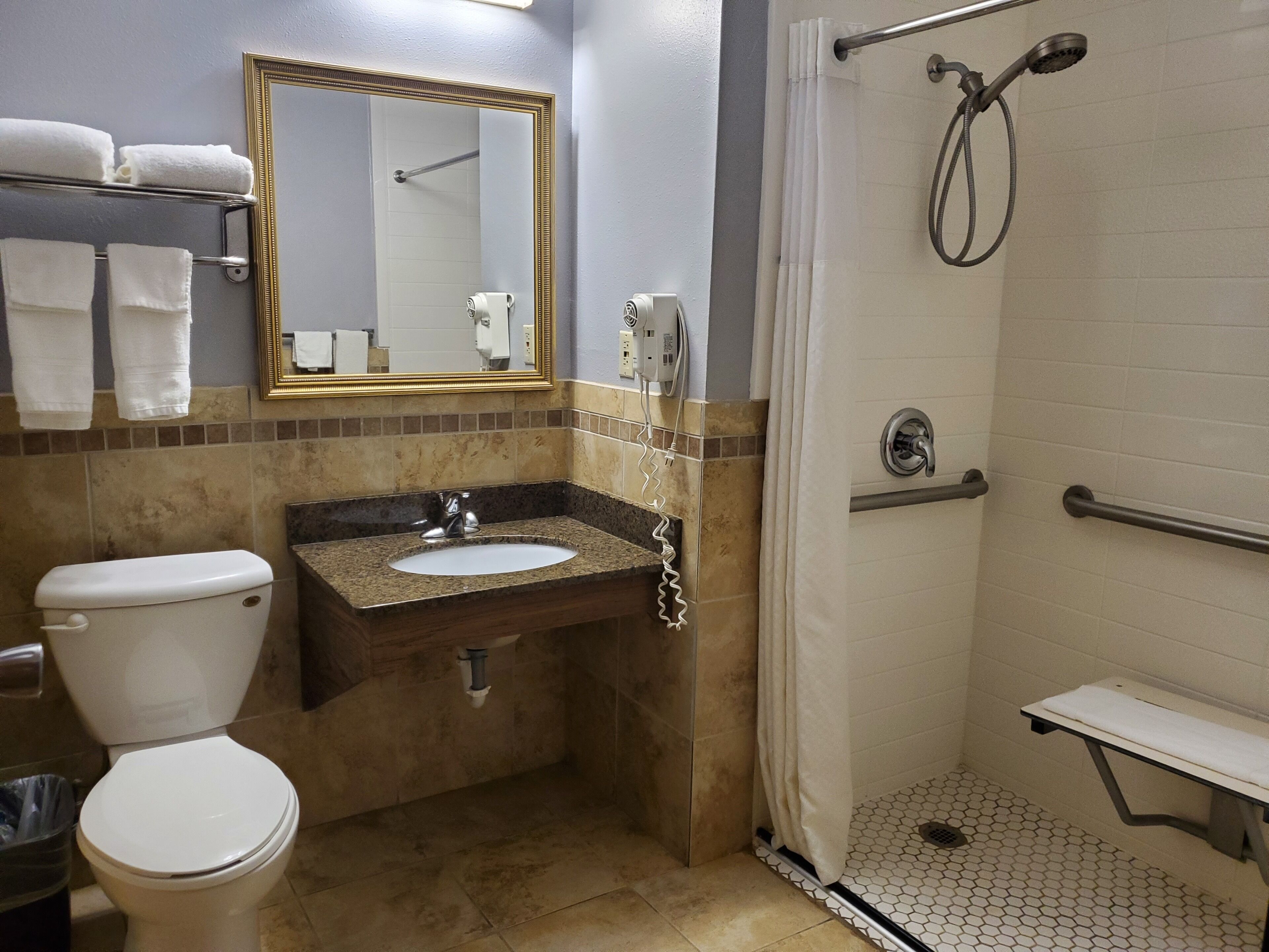 A bathroom with a toilet, sink, mirror, shower, and a towel rack.