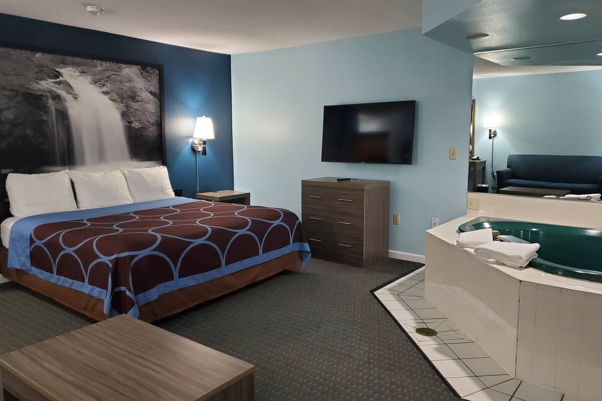 A hotel room with a bed, a desk, a dresser, a TV, a bathroom with a bathtub, and a wall mural of a waterfall.