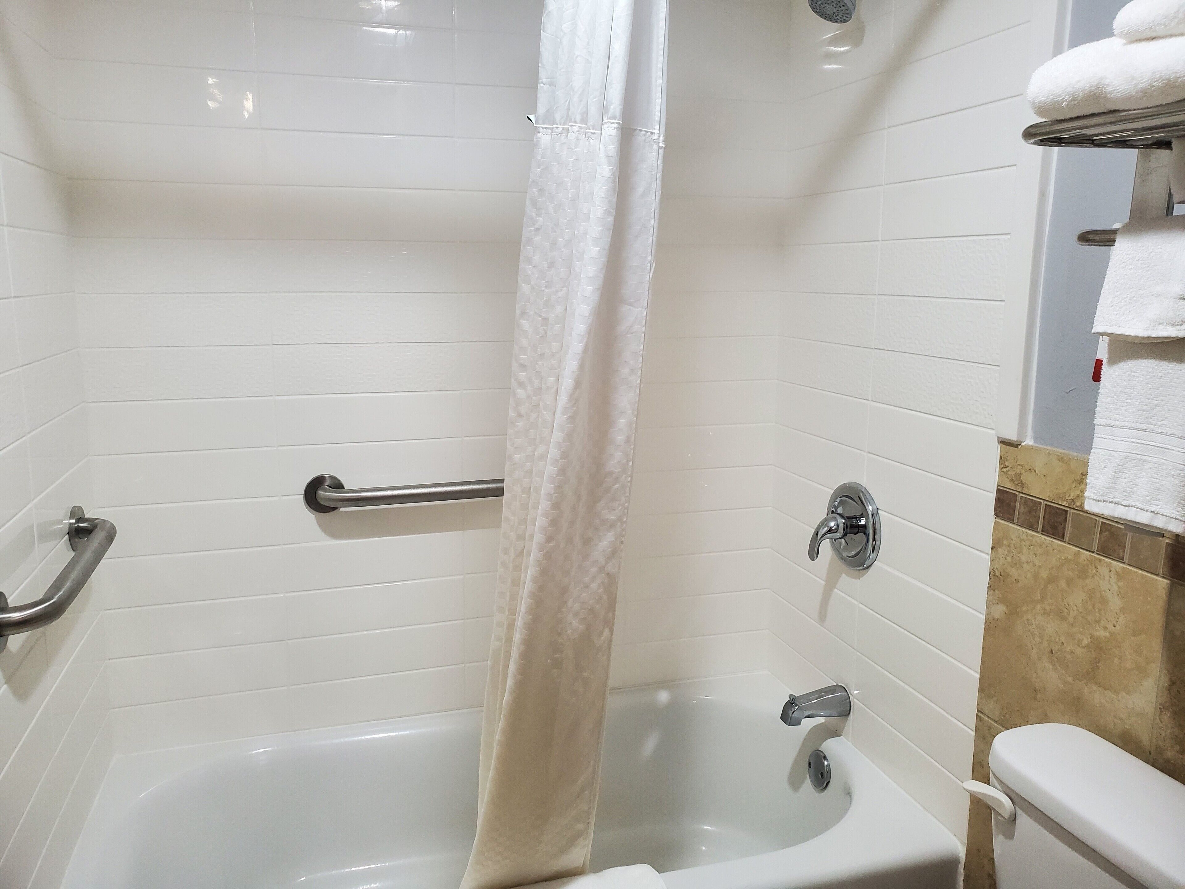Un baño con bañera, cortina de ducha, barra de apoyo y retrete.