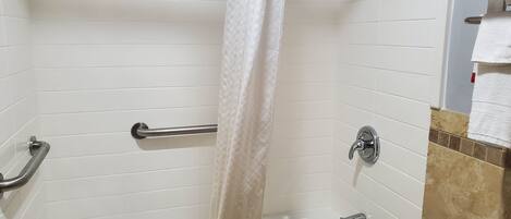 Un baño con bañera, cortina de ducha, barra de apoyo y retrete.