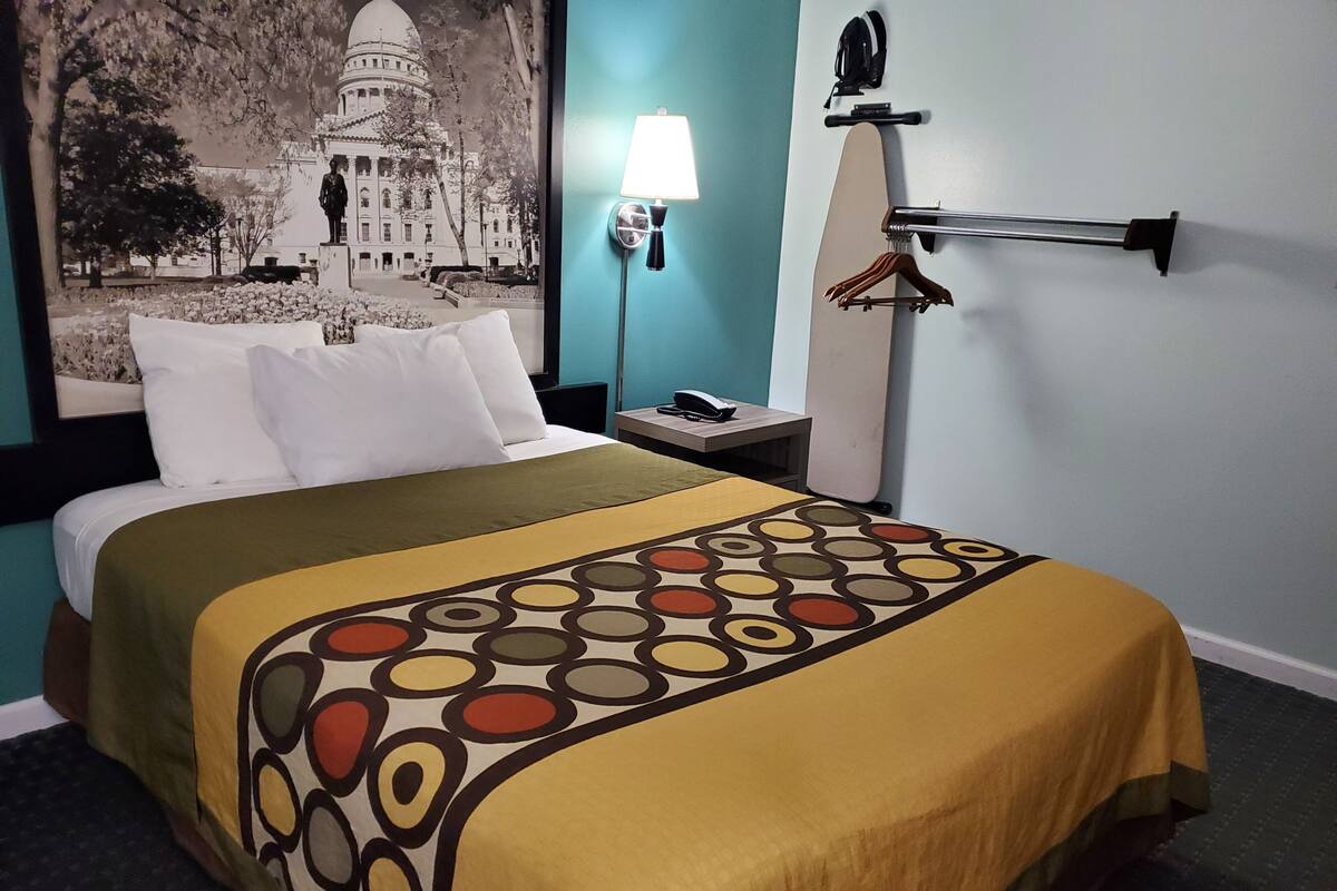 A hotel room with a bed, a nightstand, a lamp, and a wall-mounted coat rack.