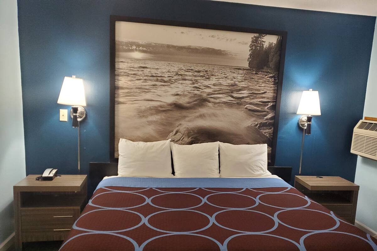 A hotel room with a large bed, two bedside lamps, a nightstand with a phone, and a wall-mounted air conditioner.