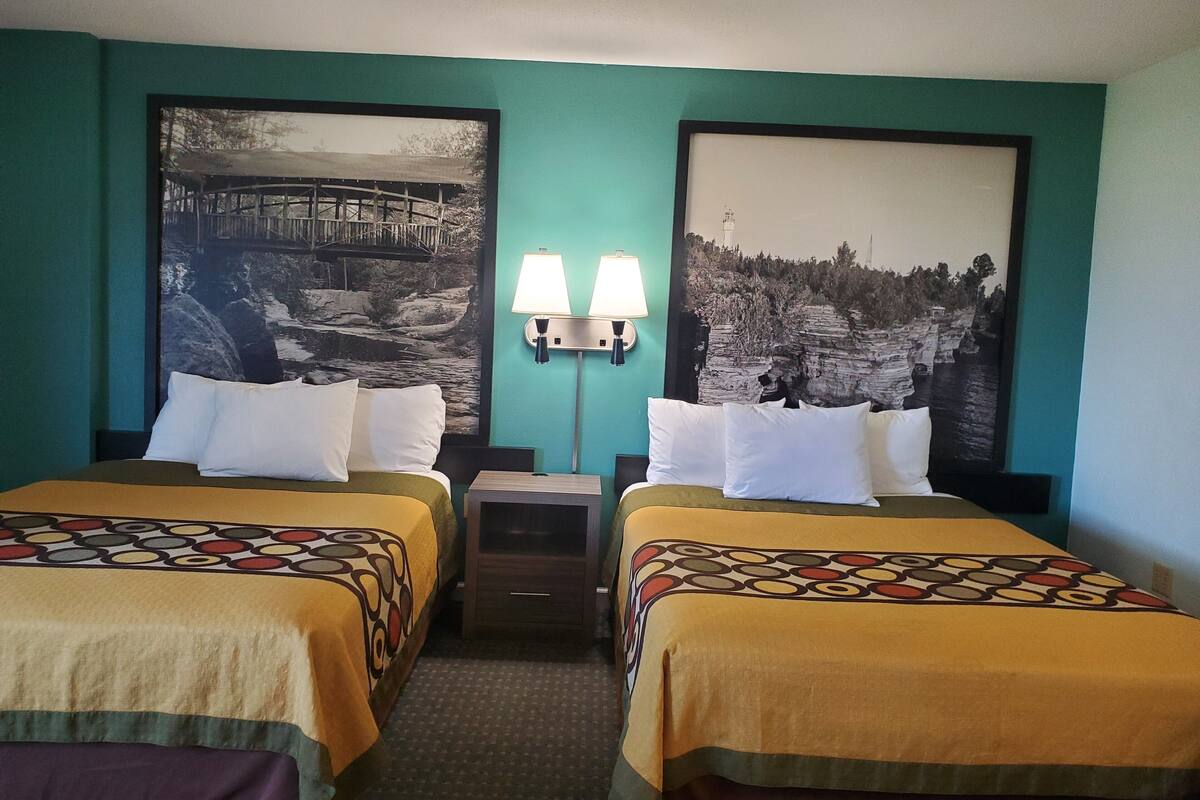 A hotel room with two beds, teal walls, and two large landscape photographs.