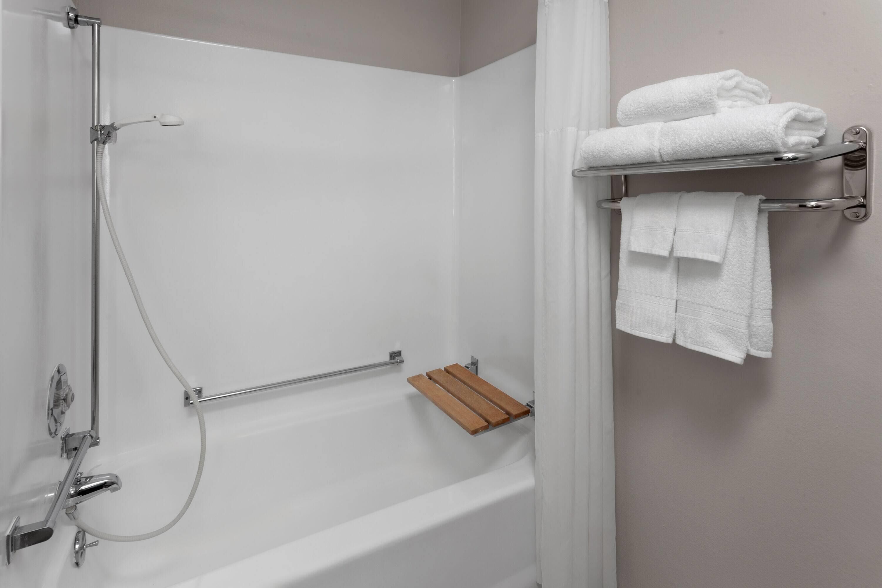 A bathroom with a bathtub, a shower, and a towel rack with folded towels.