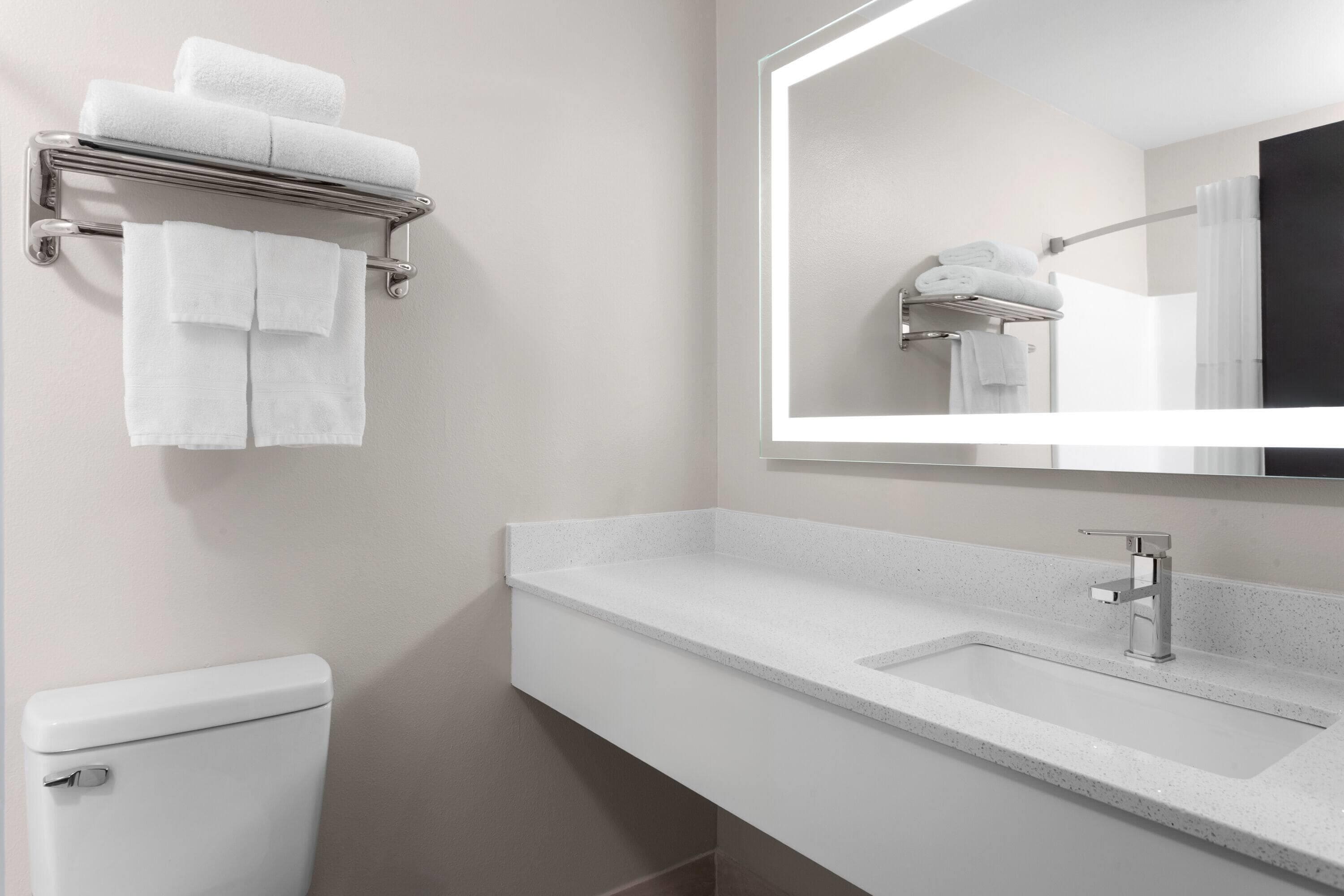 Een moderne badkamer met een toilet, een wastafel met spiegel en een handdoekrek met opgevouwen handdoeken.