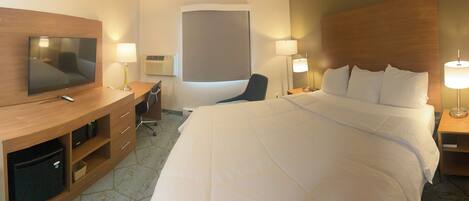 Habitación de hotel con cama, escritorio con televisor, dos lámparas de noche, una silla y ventana con persiana.