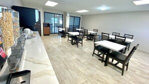 Un espace repas avec plusieurs tables et chaises, un distributeur automatique de collations et une horloge au mur.