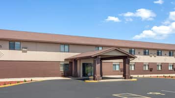 A hotel entrance with a covered waiting area, a parking lot with handicapped parking, and a building facade with multiple windows and a brick pattern.