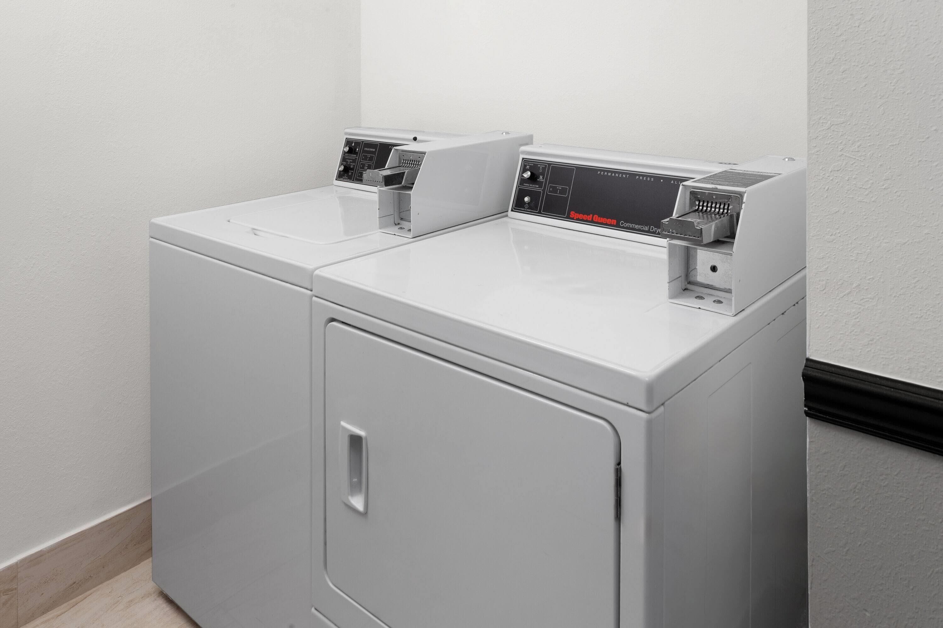 Een voorzichtszicht van een compacte, moderne wasruimte met twee gestapelde wasmachines en een droger, met bedieningspanelen en een klein bergkastje.