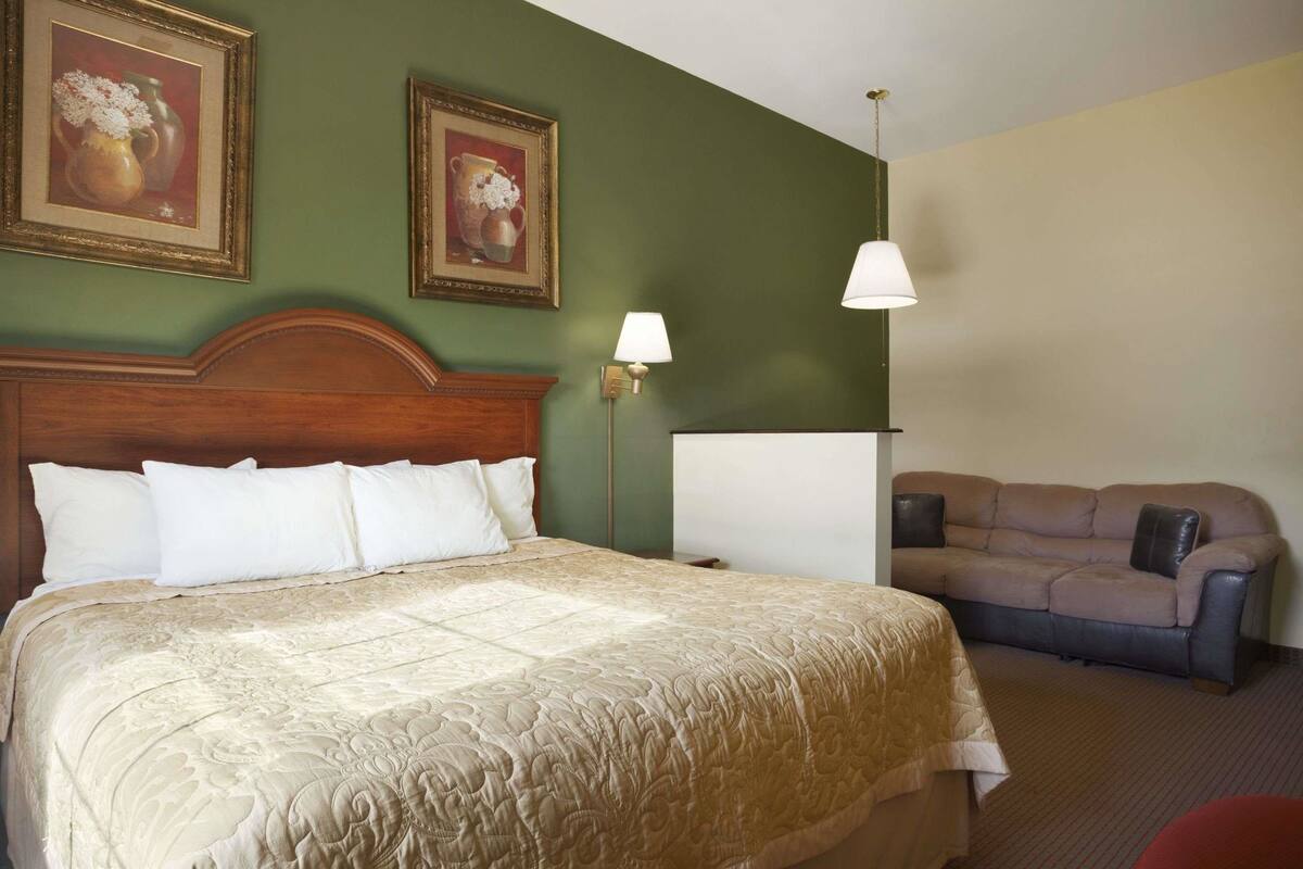 Una habitación de hotel con una cama grande, un sofá y dos lámparas fijadas a la pared.