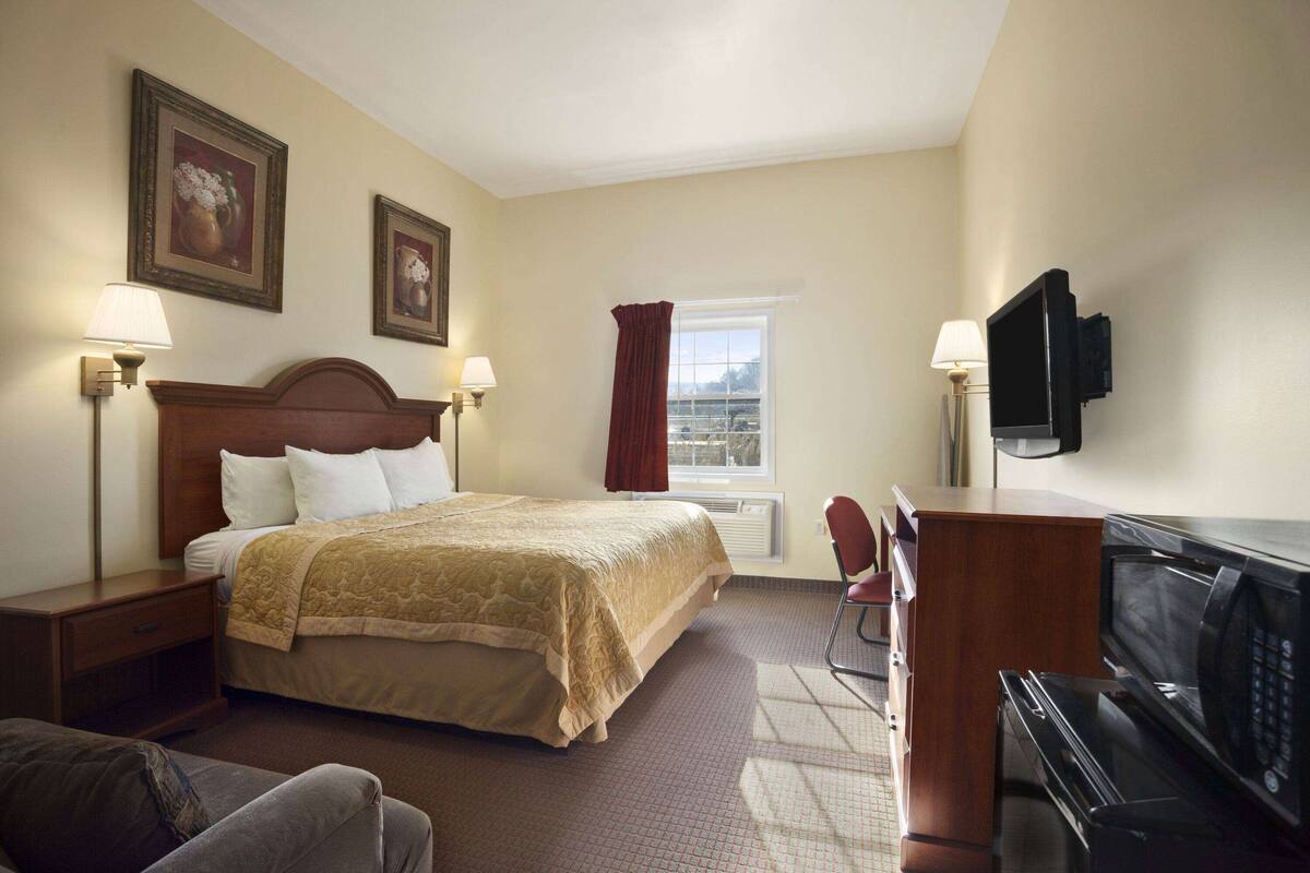 Una habitación de hotel con cama, lámparas de noche, televisor, microondas y ventana con cortinas.