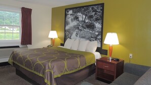 A hotel room with a bed, two bedside lamps, a nightstand, a sofa, and a large wall painting. - Super 8 by Wyndham Mifflinville Near Bloomsburg (Mifflinville)