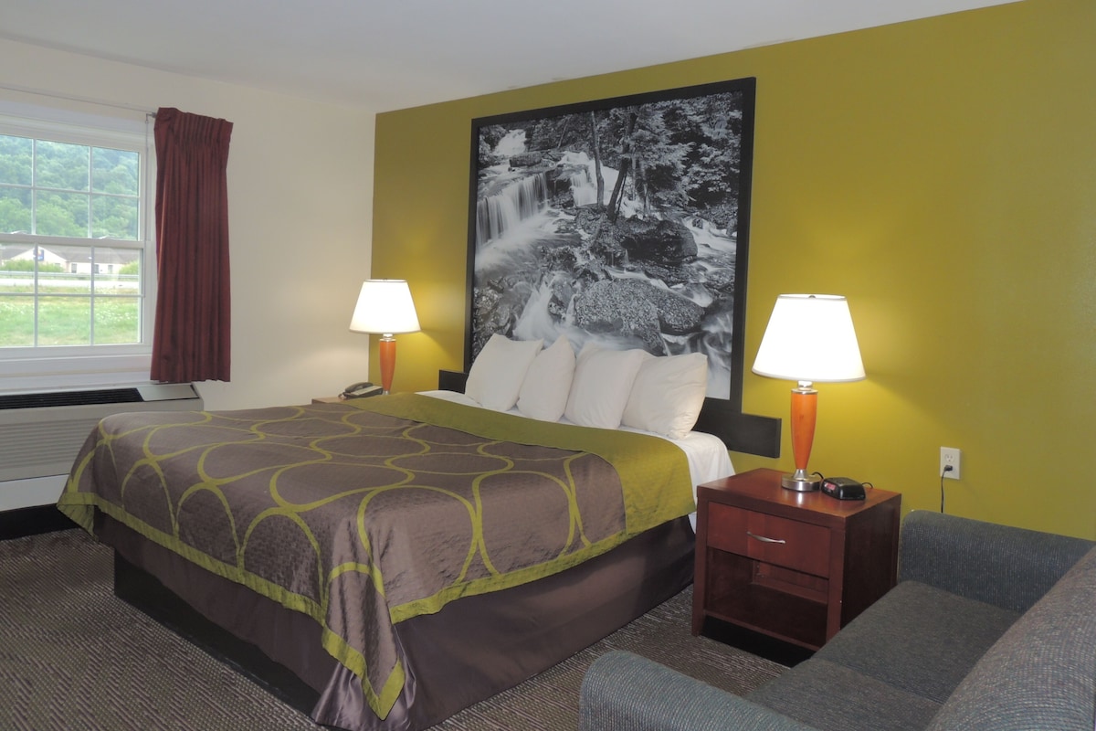Ein Hotelzimmer mit einem Bett, zwei Nachttischlampen, einem Nachttisch, einem Sofa und einem großen Wandbild.