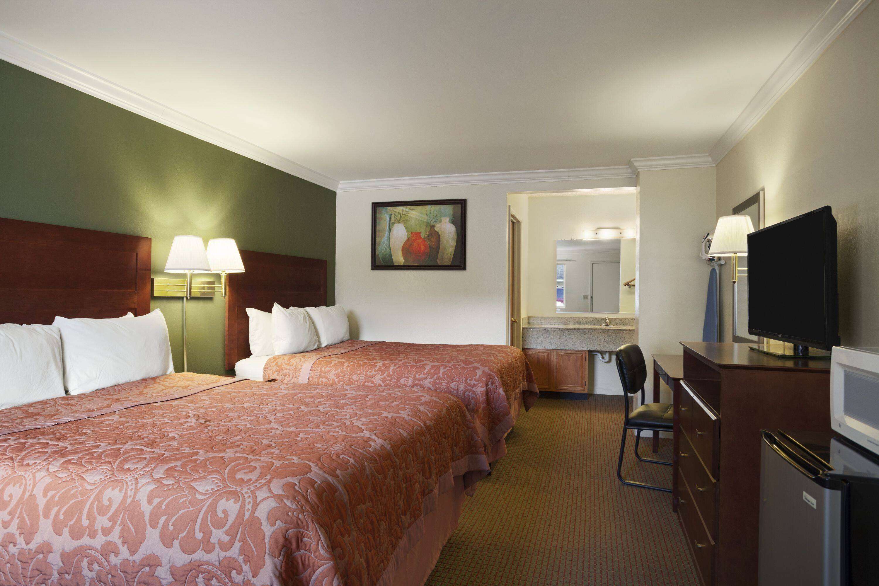 A hotel room with two beds, a desk with a television, a chair, and a small kitchenette.
