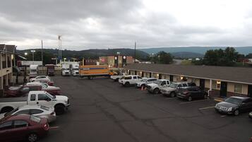 Un estacionamiento con varios coches y camiones, un motel con múltiples habitaciones y un paisaje montañoso al fondo.