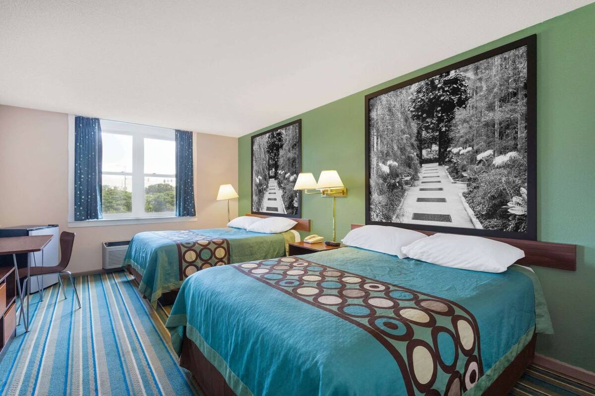 A hotel room with two beds, a desk, and a window with curtains.