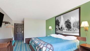 A hotel room with a bed, a desk, a chair, a hanging coat rack, and a large window with a black and white photograph of a fountain.