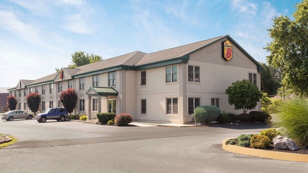 Un hotel con un cartel que indica que es un Super 8. Tiene una estructura de dos pisos con techo plano y un toldo verde sobre la entrada. Hay varias ventanas en cada piso y el edificio está rodeado de áreas ajardinadas con arbustos y árboles.