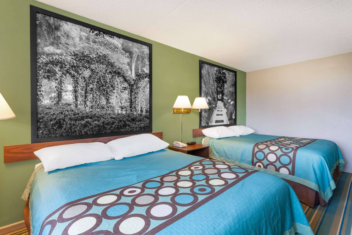 A hotel room with two beds, each with a blue bedspread and a circular pattern. There are two wall-mounted lamps on the nightstands.