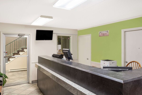 A reception area with a reception desk, a flat-screen TV mounted on the wall, a staircase leading to an upper floor, and a welcome sign on the wall.