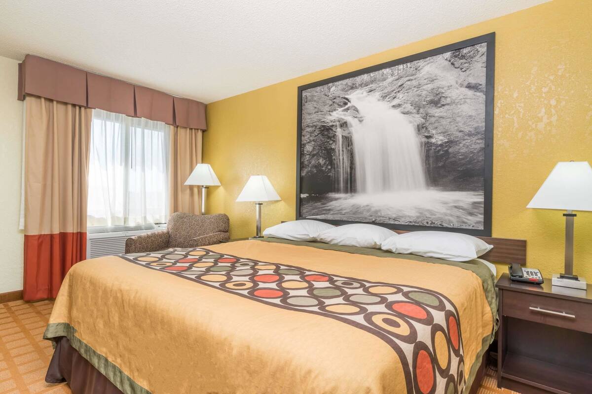 A hotel room with a large bed, two bedside lamps, a nightstand, and a large framed picture of a waterfall on the wall.