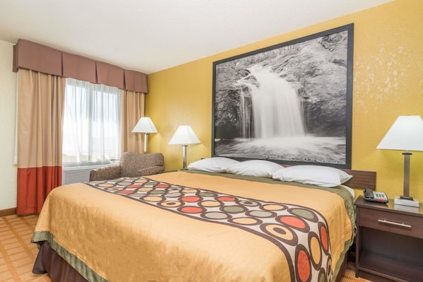 A hotel room with a large bed, two bedside lamps, a nightstand, and a large framed picture of a waterfall on the wall.