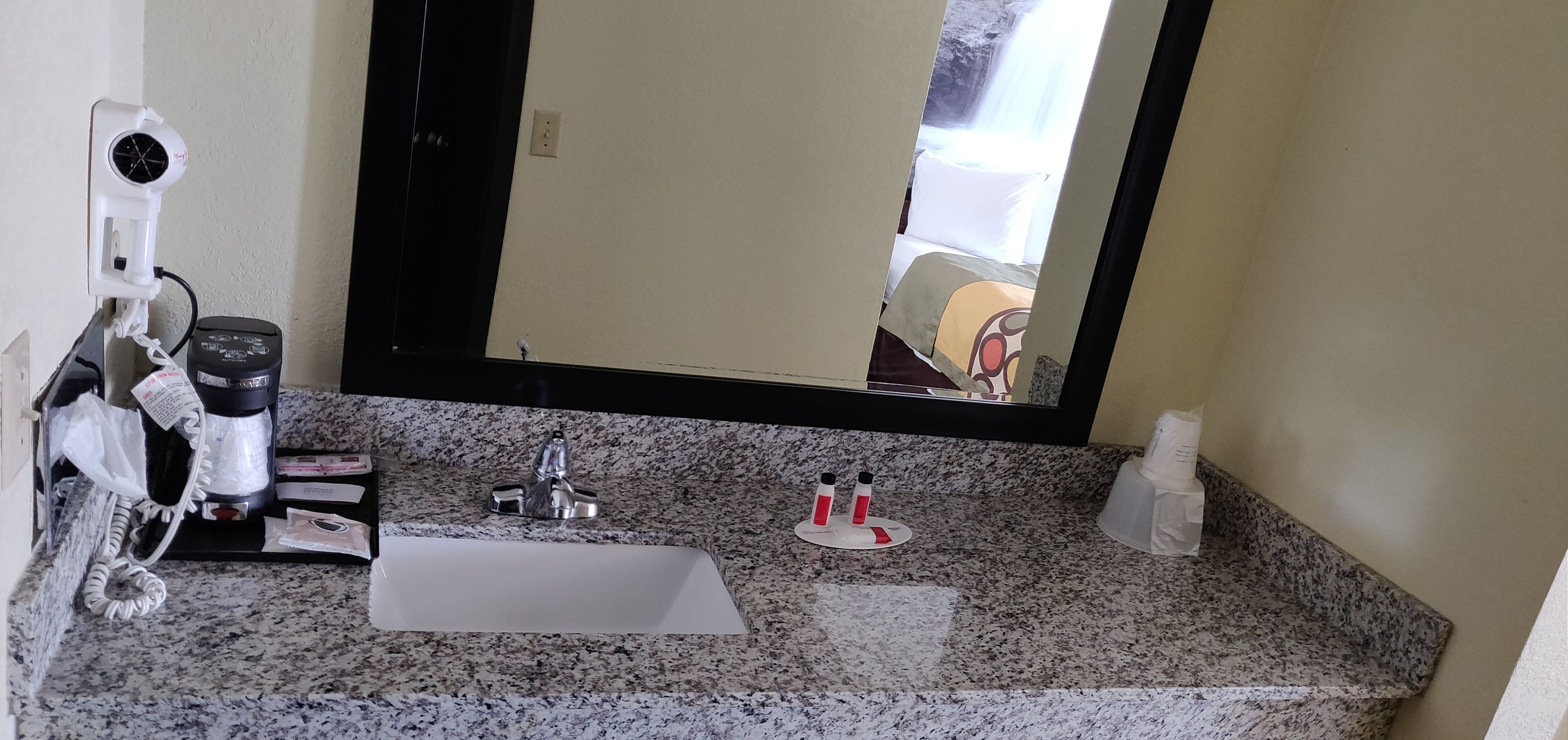 Un baño con encimera de granito, lavamanos, espejo y secador de pelo en la pared.