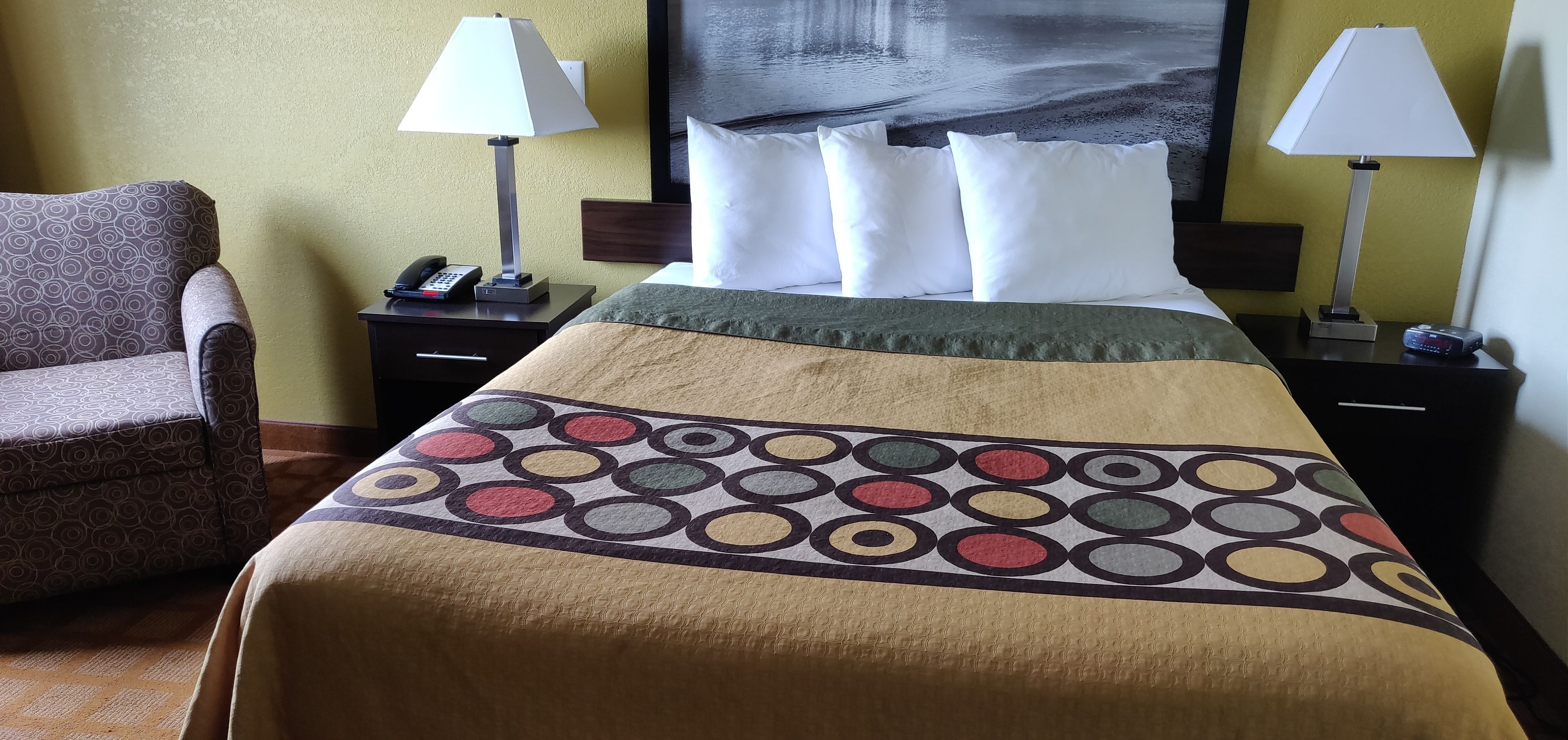 Habitación de hotel con cama, dos lámparas de noche, un teléfono y una silla.