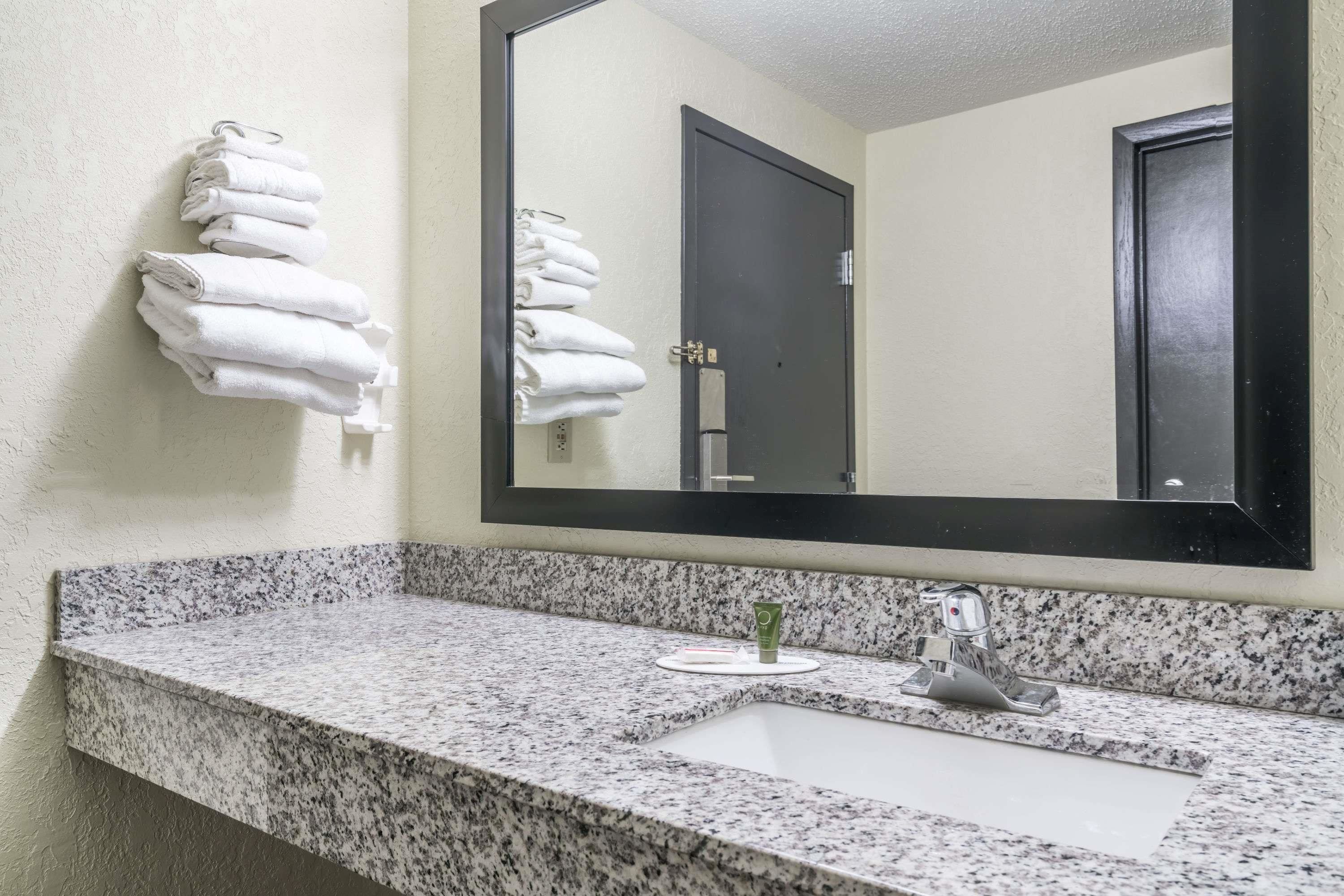 A bathroom with a granite countertop, a sink, a mirror, and a towel rack with folded towels.