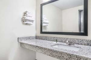 Un baño con encimera de granito, un lavabo, un espejo y una pila de toallas blancas en la pared.