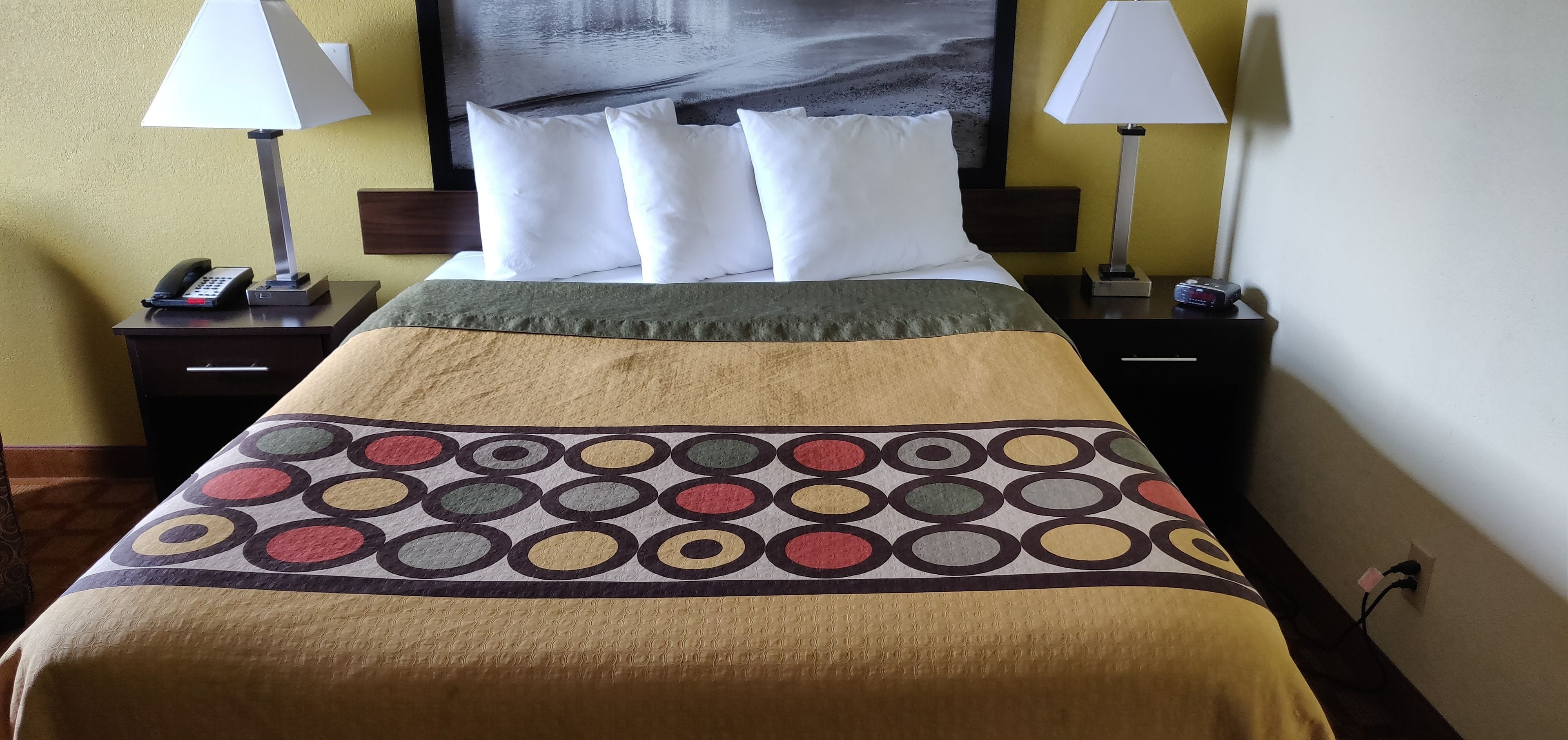 Ein Hotelzimmer mit einem Bett, zwei Nachttischen mit Lampen, einem Telefon und einem Gemälde an der Wand.