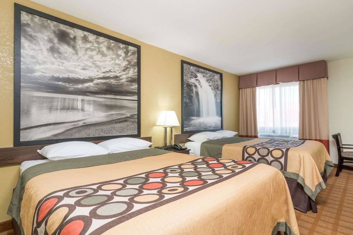 A hotel room with two beds, a large window with curtains, and artwork on the walls.
