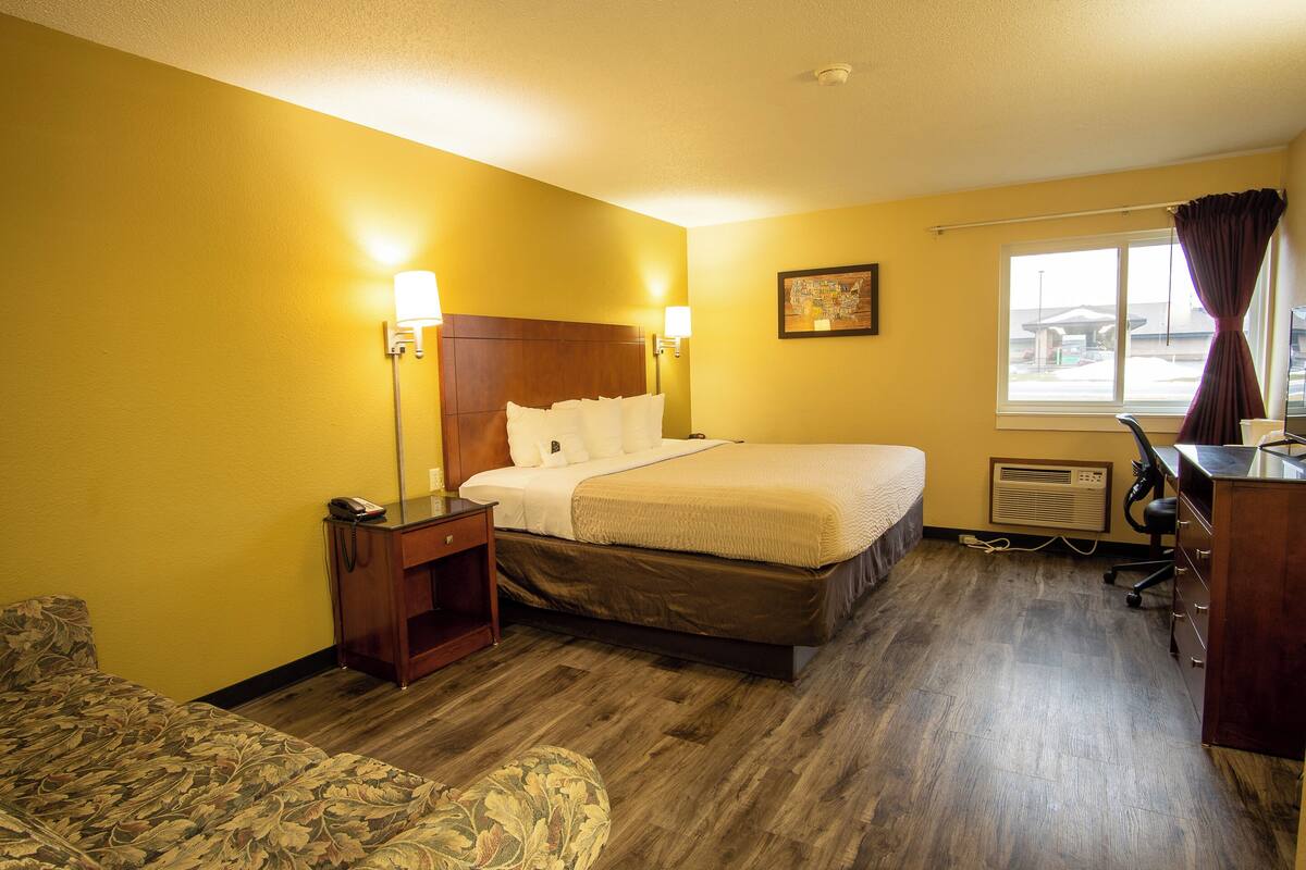 A hotel room with a bed, bedside table, lamp, and a desk with a chair.