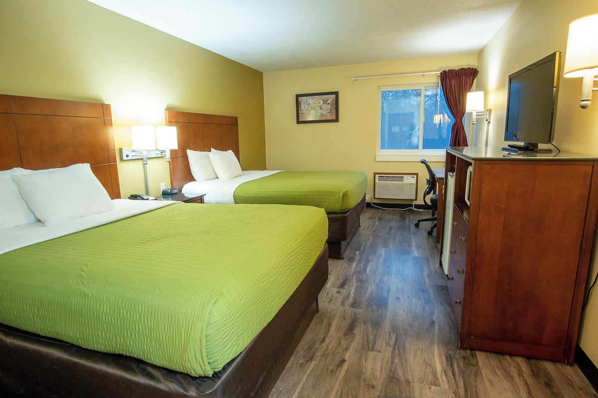 A hotel room with two beds, a desk, and a television.