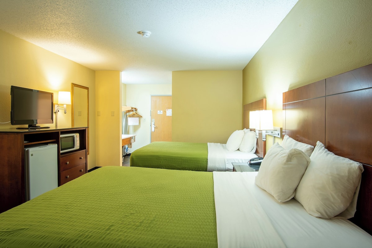 A hotel room with two beds, a TV, a mini-fridge, and a desk with a lamp.